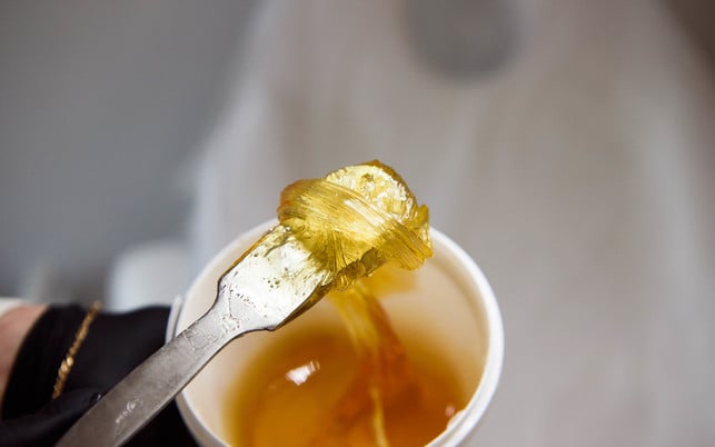 Female cosmetologist holding plastic jar with depilatory on blurred background. Depilation concept. Zuckerpaste zur Haarentfernung ist umweltfreundlicher als Enthaarunngscreme.