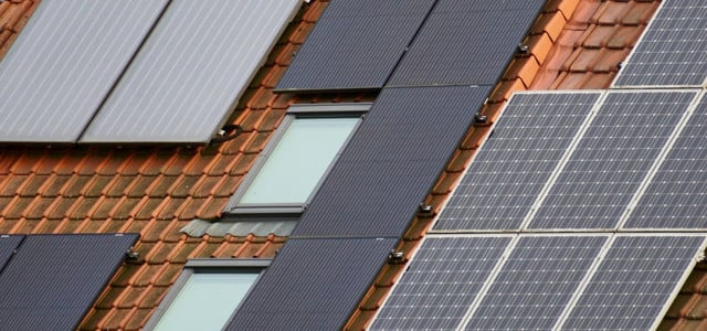 Dach mit roten Ziegeln, auf dem mehrere Solarpaneele und zwei Dachfenster installiert sind.